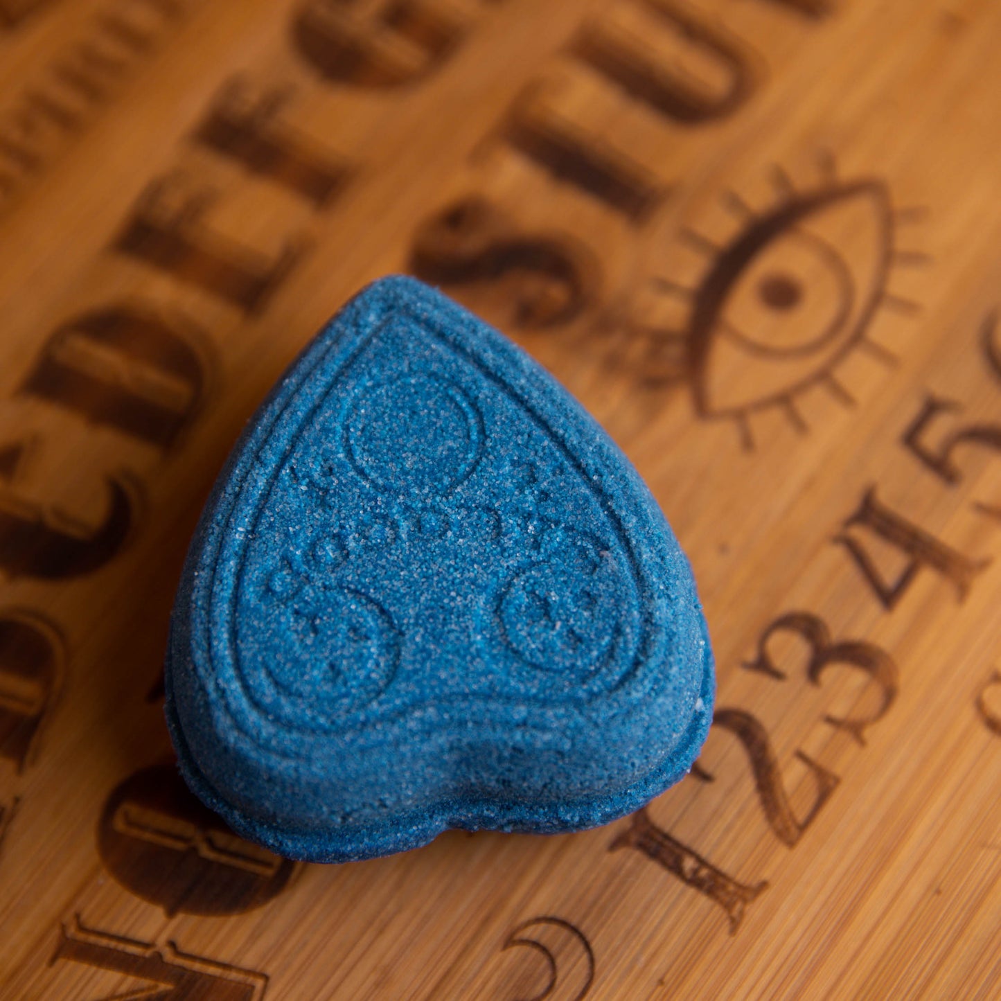 blue planchette shaped bath bomb on wooden ouija board