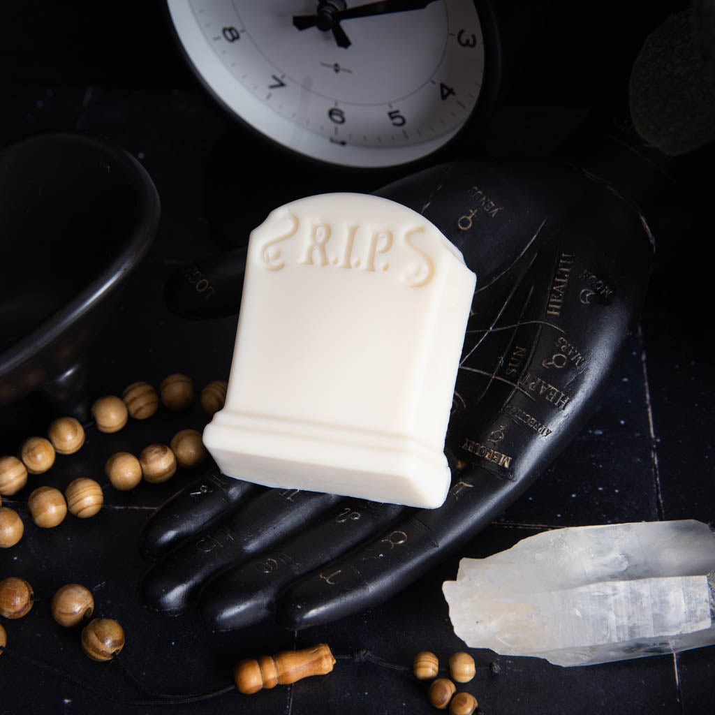 white tombstone shaped soap with "R.I.P" imprinted; on a black palmistry hand on black background